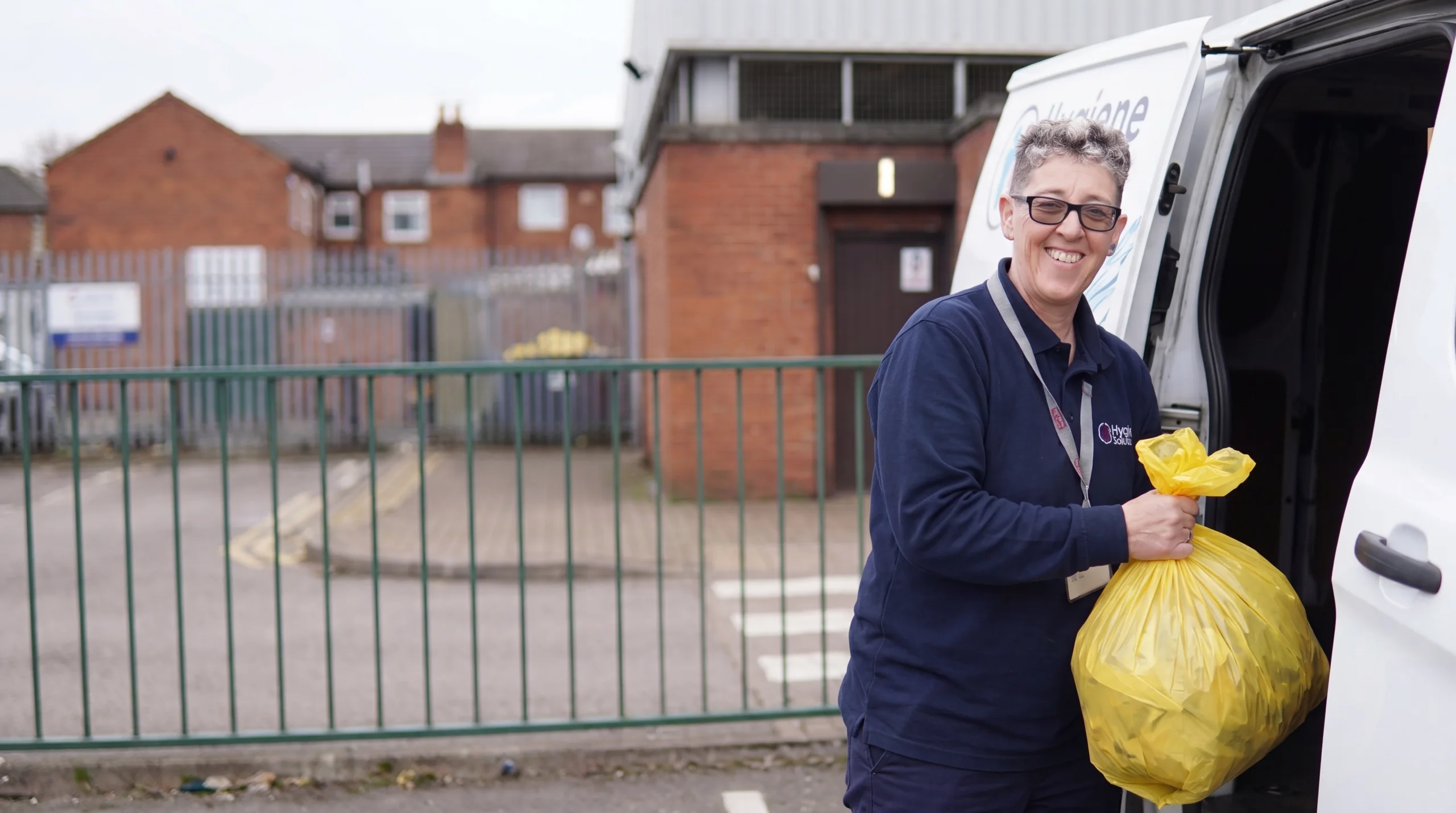 Smiling DBS-checked Hygiene Solutions team member with photo ID loading a sealed waste sack into a branded service van